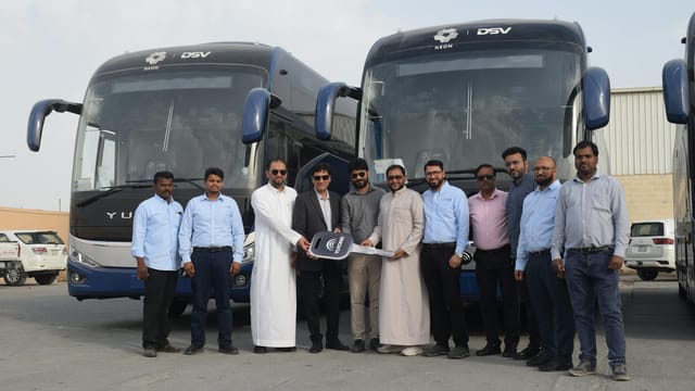 Group of businessmen standing in front of parked buses holding a large key.