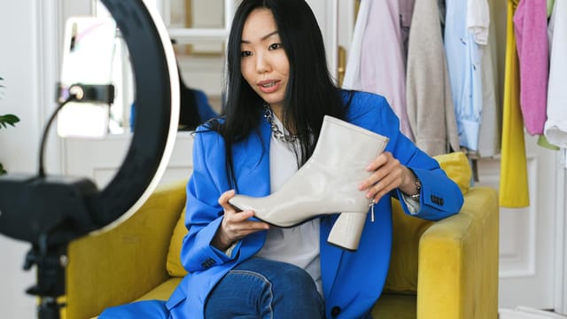 Fashion influencer streaming online reviewing shoes with smartphone and lighting ring.