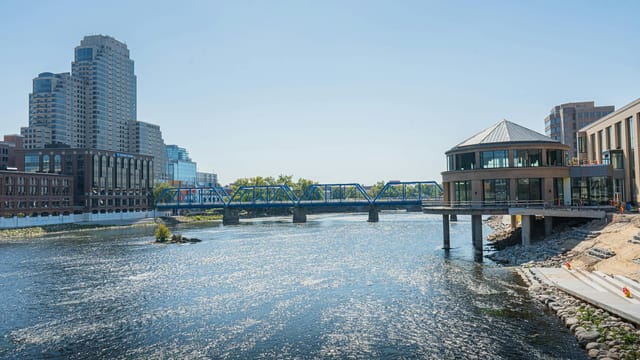 View of Grand Rapids skyline featuring the iconic Blue Bridge over a shimmering riverbank.
