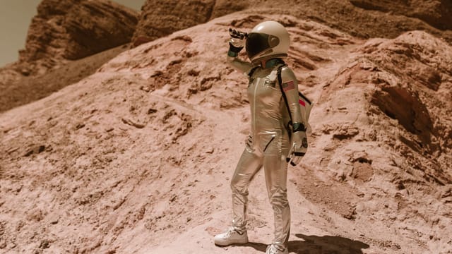 Astronaut standing on a rocky terrain resembling Mars or Moon, pondering future space exploration.