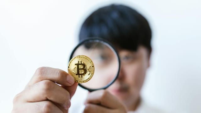 Close-up of a person examining a Bitcoin with a magnifying glass, highlighting cryptocurrency focus.