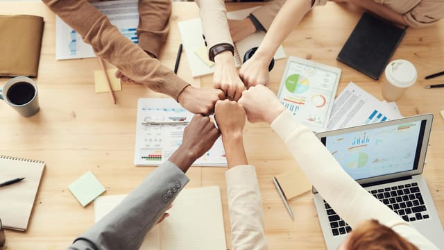 Top view of a diverse team fist bumping over a meeting table with paperwork and laptops, symbolizing teamwork.