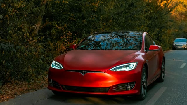Sleek red electric car driving through a scenic forest road on an autumn day.