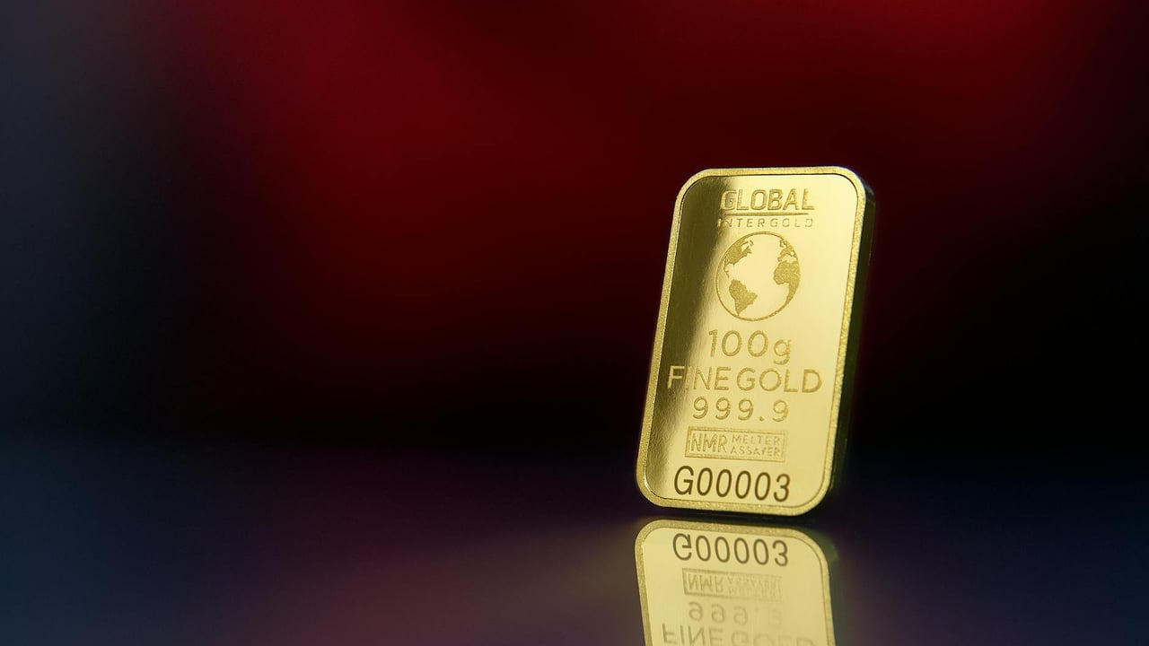 Close-up of a 100g fine gold bar against a red reflective surface, symbolizing wealth and luxury.