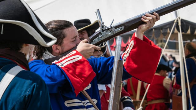 Soldiers in vibrant uniforms reenacting a historical battle with muskets outdoors.