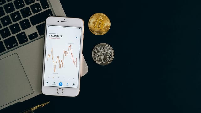 Smartphone displaying Bitcoin price chart alongside Bitcoin and Ethereum coins on black background.
