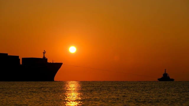 A dramatic sunset over the ocean with silhouetted ships and vivid water reflections.