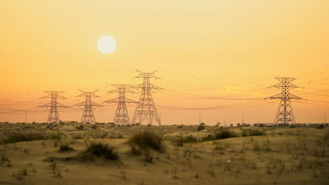 Sunset view of power lines in the Dubai desert, merging nature with technology.