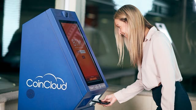 Woman smiling while using a CoinCloud cryptocurrency ATM indoors.