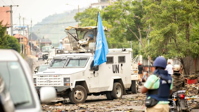 United Nations armored vehicle navigating street amid conflict. Peacekeeping and security presence.