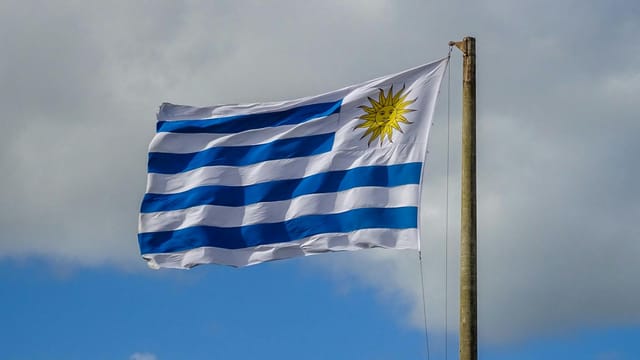 The national flag of Uruguay waves on a flagpole against a bright cloudy sky in Punta del Este.