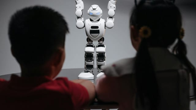 Two children observe a humanoid robot on a table, exploring technology and innovation.