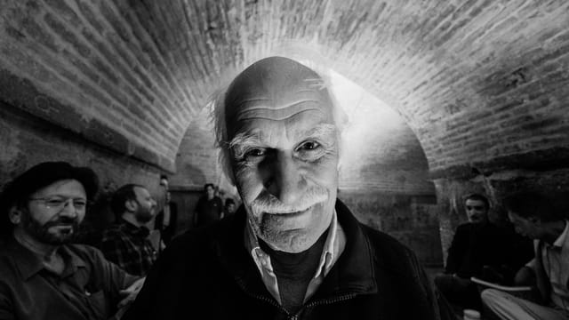 Black and white portrait of an elderly man with a moustache, smiling in Isfahan, Iran.