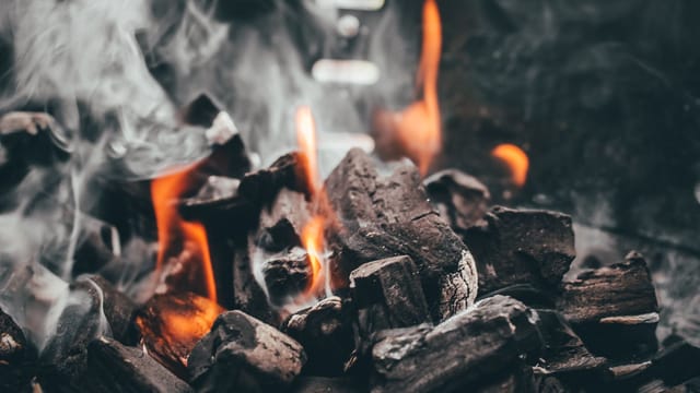 Captivating close-up of charcoal engulfed in flames and smoke, creating a fiery display.