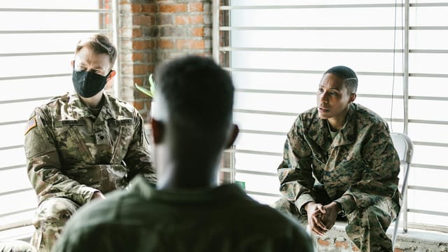 Military veterans participate in a supportive group therapy session indoors for mental health recovery.