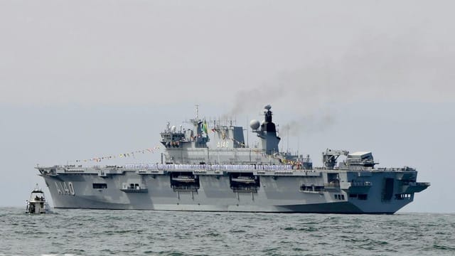 Military aircraft carrier sailing on ocean with visible smoke.