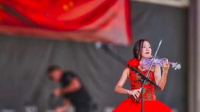 A talented violinist performs on stage in a vibrant red dress during a cultural festival.