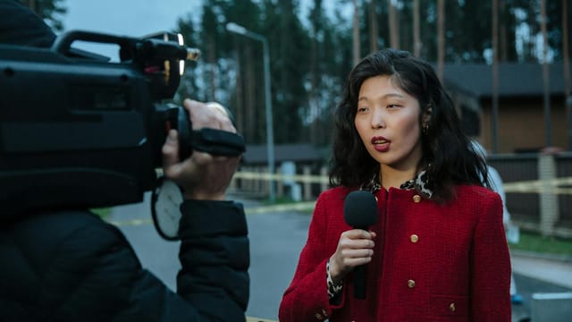 Asian female journalist reporting live from a suburban crime scene with camera and microphone.