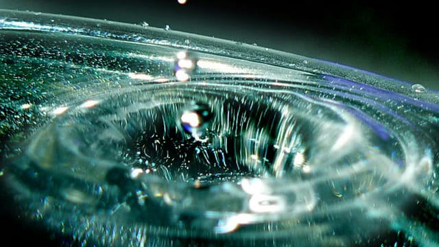 Close-up view of a water droplet creating ripples in a pool of water, capturing the moment of impact.