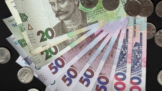 Close-up of assorted Ukrainian banknotes and coins on a dark background.