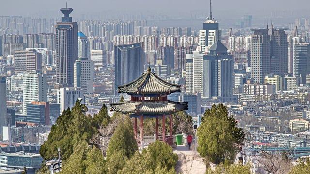 Elevated view of Jinan's skyline with traditional Chinese pavilion in the foreground.