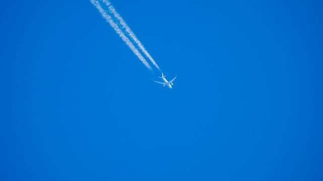 A commercial airplane leaves contrails as it flies high through a clear blue sky.
