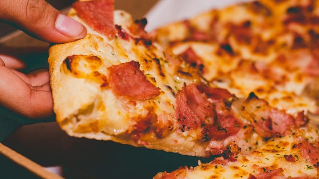 Close-up of a hand holding a delicious slice of pepperoni pizza.