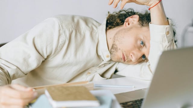 A tired Caucasian man at a desk, showing signs of exhaustion and stress, exemplifying workplace burnout.
