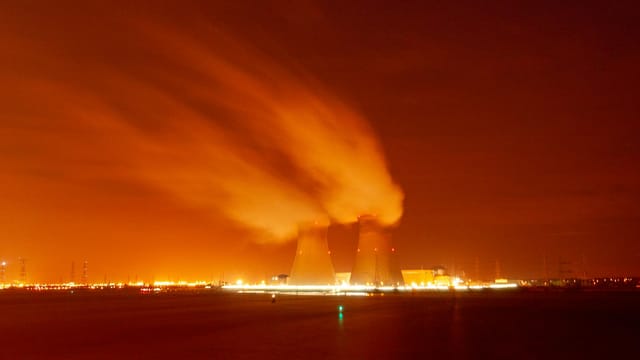 A dramatic view of cooling towers emitting steam against an orange night sky, showcasing industrial energy production.