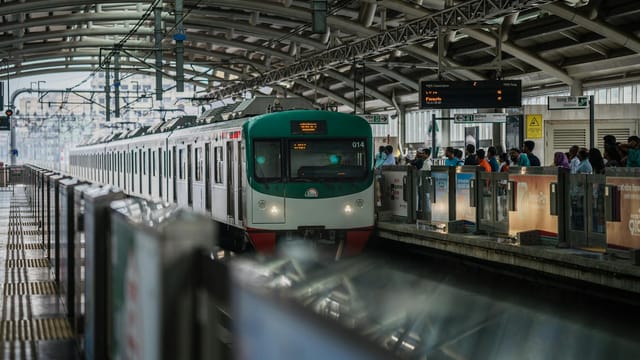 Modern metro train at Dhaka station with commuters waiting on platform, showcasing public transport in Bangladesh.