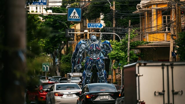 A towering robot statue stands amidst bustling traffic on a street in Bangkok, Thailand.