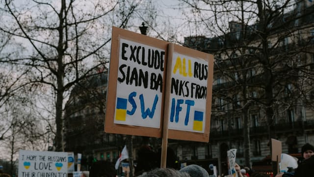 Crowd gathered with placards during a protest against Russian banks in an urban setting.