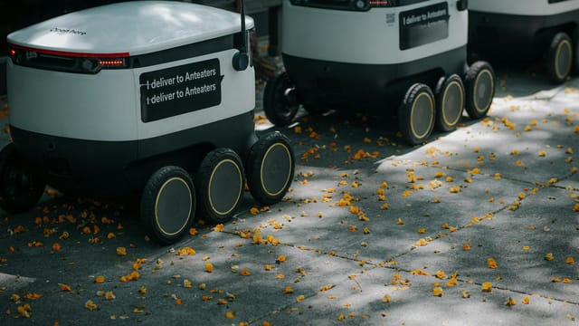 Futuristic delivery robots navigating a leaf-strewn sidewalk, showcasing innovation in modern urban logistics.