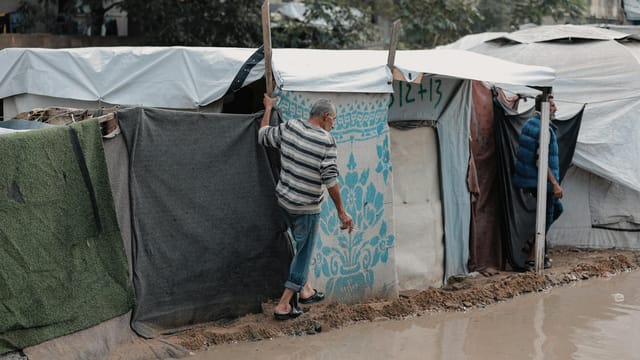 A man navigates a muddy path in a makeshift shelter area in Gaza, reflecting resilience and hardship.