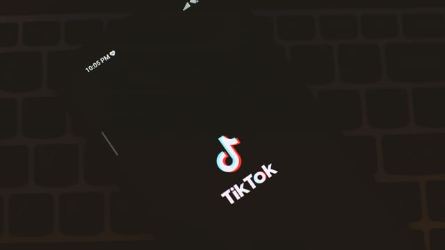 Close-up of a smartphone displaying the TikTok app logo against a dark keyboard background.
