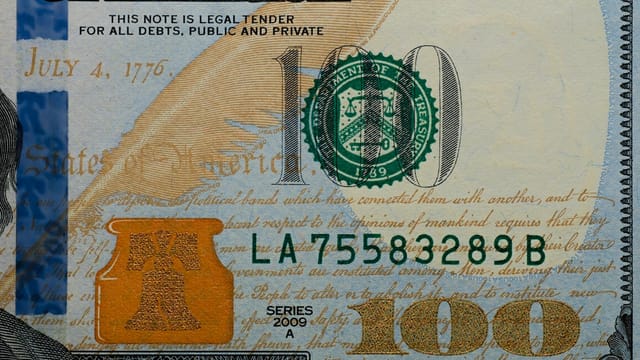 Detailed view of a US 100 dollar bill highlighting security features and design elements.