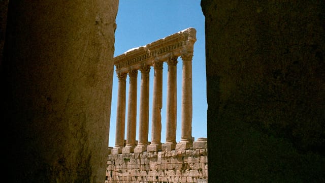 View of ancient Roman columns framed between stone walls, evoking a vintage aesthetic.