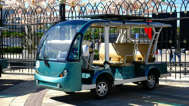 Modern electric shuttle parked in a scenic urban park setting under sunny skies.