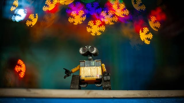 Toy robot capturing colorful bokeh lights in a vibrant, festive indoor setting.