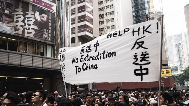 Protesters in Hong Kong holding banners against extradition to China, urban backdrop.