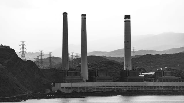 Black and white photo of a large industrial power plant in Taiwan with smoke stacks against a mountainous backdrop.
