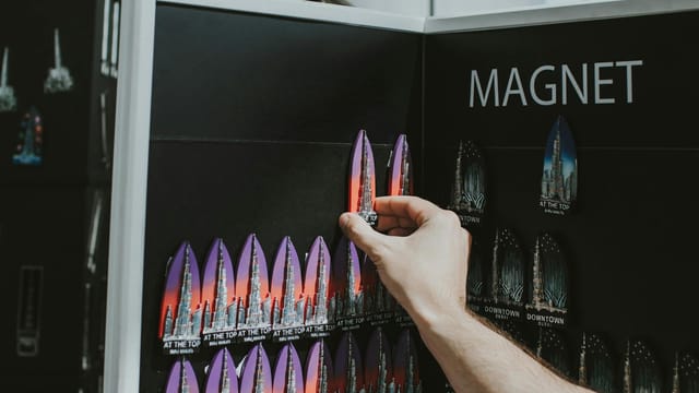 A hand selecting colorful Burj Khalifa souvenir magnets from a display in Dubai shop.