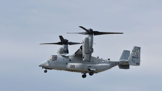 A V-22 Osprey military aircraft flying in a clear sky, showcasing its unique tiltrotor capability.