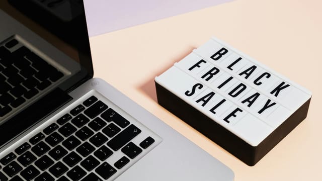 A laptop beside a lightbox sign with 'Black Friday Sale' for online shopping promotions.