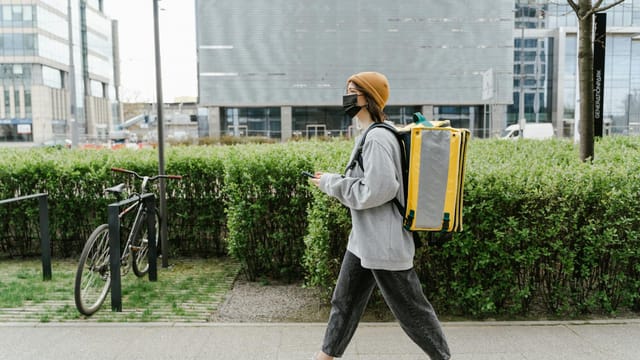 A delivery person walking through Warsaw with a yellow thermal bag, providing urban food delivery services.