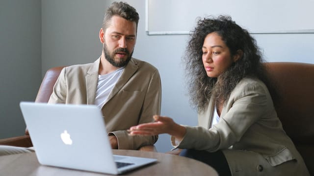 Serious colleagues in stylish outfits sitting at table and using laptop while discussing new project in office
