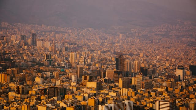 A sprawling view of Tehran's urban landscape with mountains in the background at sunset.