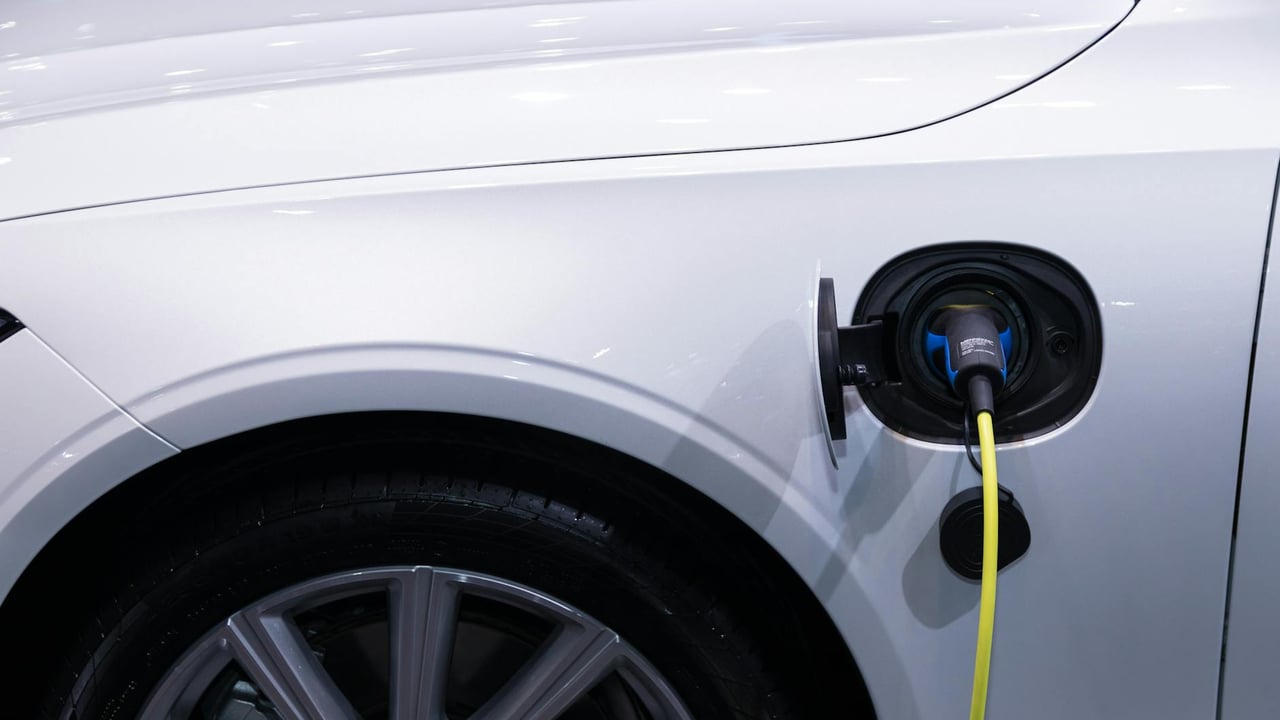 A white electric car is plugged in for charging, close-up view of the charging port.