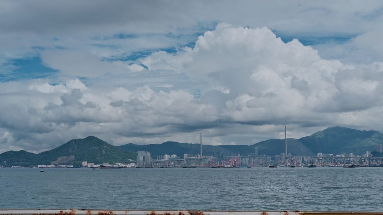 Dramatic cityscape with ocean and mountains under cloudy sky.