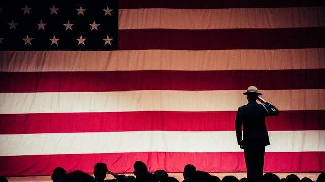 A solemn moment as a soldier salutes the American flag during a ceremony inside an auditorium.
